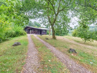 A gravel driveway leading to a wooden cabin surrounded by grass trees and bushes at The Log Cabin in Sheldon Blackdown Hills