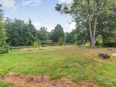A grassy garden area with trees and large rocks at The Log Cabin in Sheldon Blackdown Hills