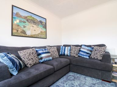 A corner sofa with blue and patterned cushions in a living room with a framed picture on the wall at Savoy View in Mullion