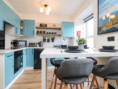 A kitchen with blue cabinets a white countertop and a dining table set with black plates and glasses at Savoy View in Mullion