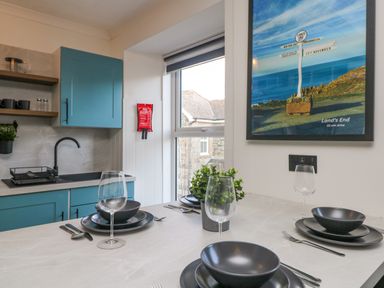 A kitchen with blue cabinets black sink and faucet dining table set with black dishes glasses and cutlery at Savoy View in Mullion