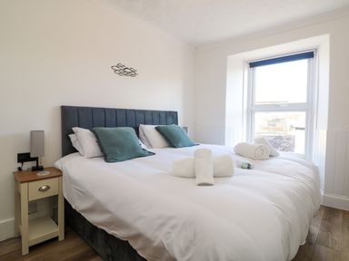 A bedroom with a double bed two teal pillows bedside table with lamp and a window at Savoy View in Mullion