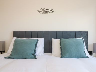 A bed with two green pillows and white bedding against a wall with fish wall art at Savoy View in Mullion