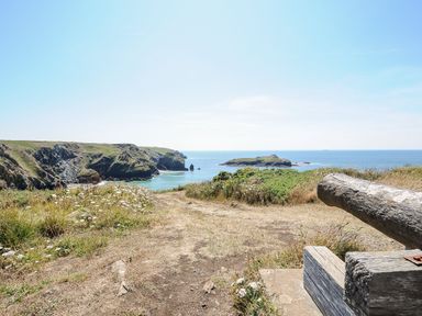 A coastal landscape with cliffs and a wooden bench overlooking the ocean at Savoy View in Mullion