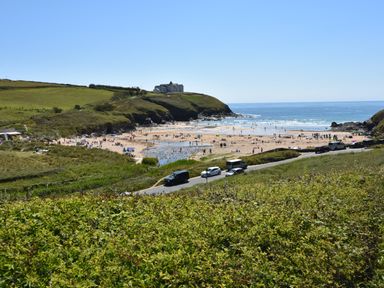 A beach with people on the sand and in the water near a coastal road with cars and green hills at Savoy View in Mullion