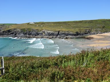 A coastal bay with surfers in the water and people on a sandy beach with cliffs and grassland in the background at Savoy View in Mullion