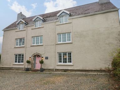 A large house with multiple white windows and a pink front door with two potted plants at Norchard Farm House in Redberth near St Florence