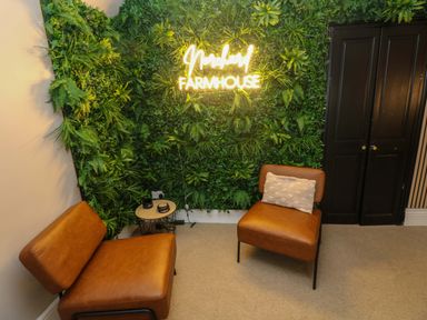 A sitting area with two brown chairs a small table and a green plant wall with a lit sign saying Norchard Farmhouse at Norchard Farm House Redberth near St Florence