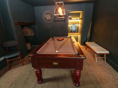 A game room with a pool table, darts board on the wall, a chair, and a bench at Norchard Farm House Redberth near St Florence