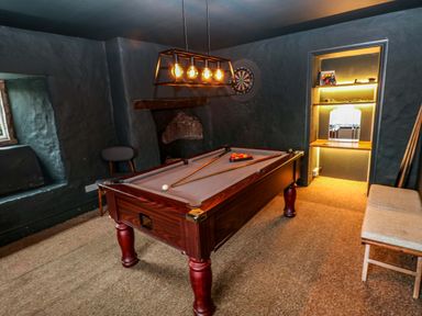 A game room with a pool table, dartboard on the wall, chair, and bench at Norchard Farm House Redberth near St Florence