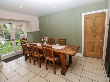 A dining room with a wooden table and chairs next to garden doors at Norchard Farm House Redberth near St Florence