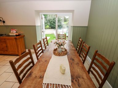 A wooden dining table with chairs set in a dining area with green paneled walls and an open door leading to a garden at Norchard Farm House in Redberth near St Florence