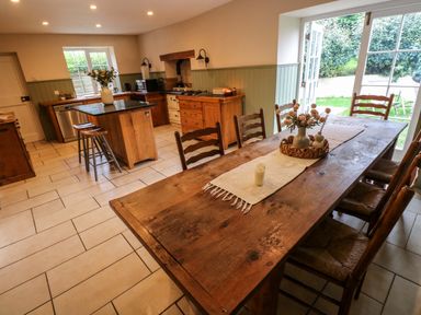 A kitchen with a wooden dining table and chairs a kitchen island with stools and open doors leading outside at Norchard Farm House Redberth near St Florence