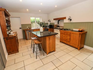 A kitchen with wooden cabinets island with stools and tiled floor at Norchard Farm House in Redberth near St Florence