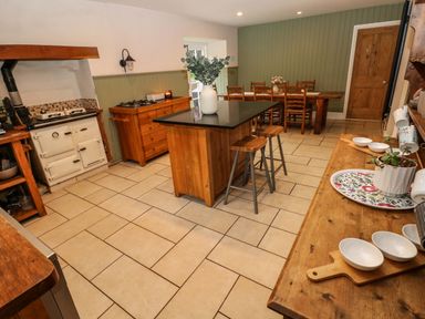 A kitchen with a central island and stools a wooden dining table with chairs and an old-fashioned stove at Norchard Farm House Redberth near St Florence