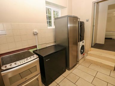 A kitchen area with stove freezer refrigerator washing machine and dryer near steps at Norchard Farm House in Redberth near St Florence