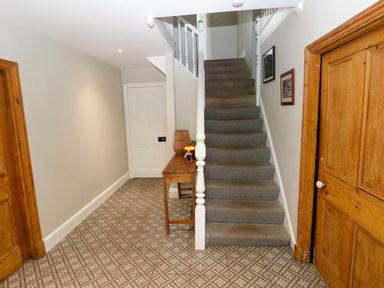 A hallway with gray carpeted stairs a wooden table with items on it patterned floor tiles and wooden doors at Norchard Farm House in Redberth near St Florence