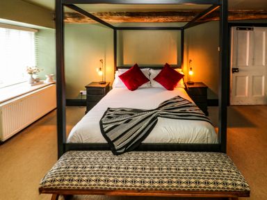 A bedroom with a four poster bed with red pillows and black side tables with lamps at Norchard Farm House Redberth near St Florence