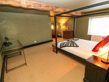 A bedroom with a canopy bed a glass table a wooden chest of drawers and a floor lamp at Norchard Farm House in Redberth near St Florence