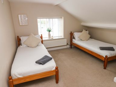 A bedroom with two single beds each with a pillow and towel and a window with blinds and a vase with flowers at Norchard Farm House in Redberth near St Florence