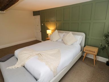 A bedroom with a bed and pillows against a green paneled wall and bedside tables at Norchard Farm House in Redberth near St Florence