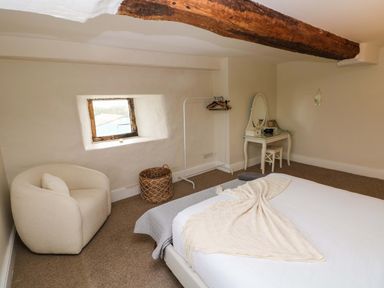 A bedroom with a bed a white armchair a woven basket a dressing table with a mirror and a wooden beam on the ceiling at Norchard Farm House Redberth near St Florence