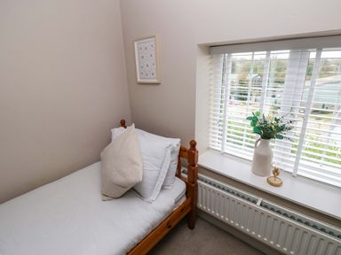 A small bedroom with a single wooden bed a white pillow a beige cushion a framed picture on the wall and a window with blinds and a vase with green plants on the windowsill at Norchard Farm House in Redberth near St Florence