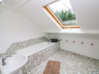 A bathroom with a bathtub a sink a skylight window and tiled floor and walls at Norchard Farm House Redberth near St Florence