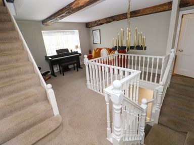 A landing area with beige carpet stairs a black piano an orange sofa with cushions wooden ceiling beams and white painted banisters at Norchard Farm House in Redberth near St Florence