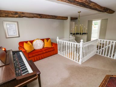 A seating area with an orange sofa and pillows next to a piano and white stair railing at Norchard Farm House in Redberth near St Florence