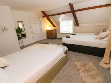 A bedroom with two beds a wooden chest of drawers a standing mirror a plant and exposed wooden beams at Norchard Farm House in Redberth near St Florence