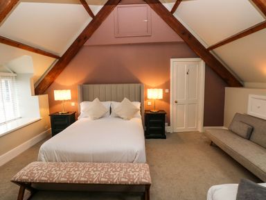 A bedroom with a double bed with pillows two bedside tables with lamps a bench at foot of bed a sofa and attic beams at Norchard Farm House Redberth near St Florence