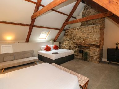 A bedroom with two beds a beige sofa a stone fireplace and wooden beams at Norchard Farm House Redberth near St Florence