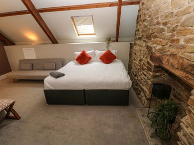 A bedroom with a bed with two orange pillows a gray sofa a stone wall and a skylight window at Norchard Farm House Redberth near St Florence