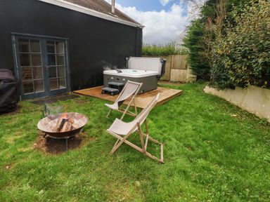 A garden area with a hot tub on a wooden platform two chairs and a fire pit in the grass at Norchard Farm House Redberth near St Florence