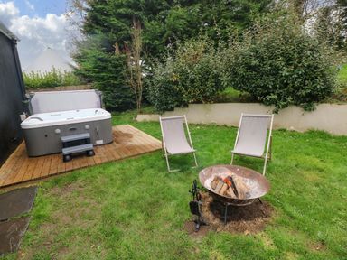 A garden with a fire pit and two chairs next to a hot tub on a wooden deck at Norchard Farm House in Redberth near St Florence