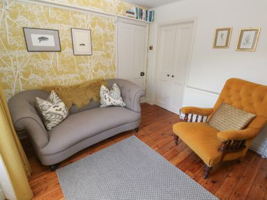 A sitting room with a grey sofa and a mustard armchair on wood floors at Apple Tree Cottage in Gweek