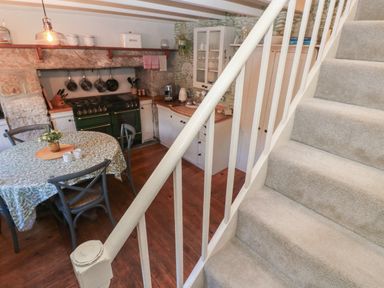 A kitchen with a dining table four chairs stove hanging pans and carpeted stairs at Apple Tree Cottage in Gweek