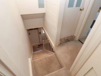 A carpeted staircase leading down from a hallway with closed doors at Apple Tree Cottage in Gweek