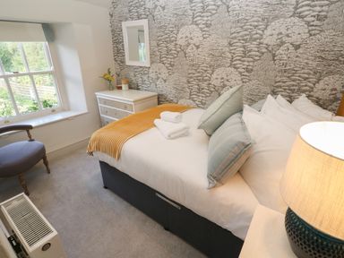 A bedroom with a bed with pillows and folded towels a chair a chest of drawers and a lamp at Apple Tree Cottage in Gweek