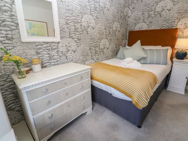 A bedroom with a double bed with striped pillows and a yellow blanket next to a white chest of drawers with flowers at Apple Tree Cottage in Gweek