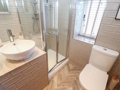 A bathroom with a toilet sink with faucet glass shower enclosure and a window with blinds at Apple Tree Cottage in Gweek