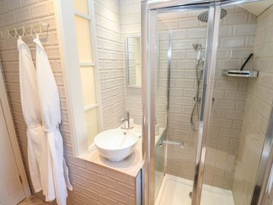 A bathroom with a glass shower enclosure a round sink on a counter and two white robes hanging on hooks at Apple Tree Cottage in Gweek