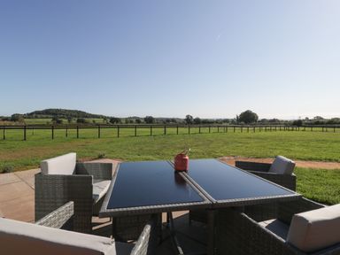 An outdoor patio table with chairs overlooking a fenced grassy field at Leadon View Willow in Upleadon near Newent