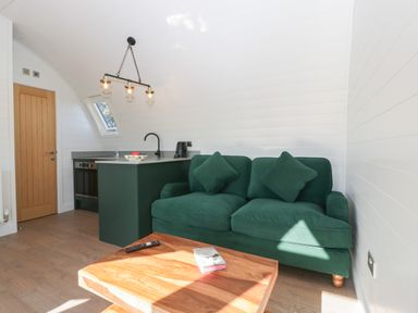 A small living room with a green sofa, wooden coffee table, and kitchen area at Leadon View Willow in Upleadon near Newent