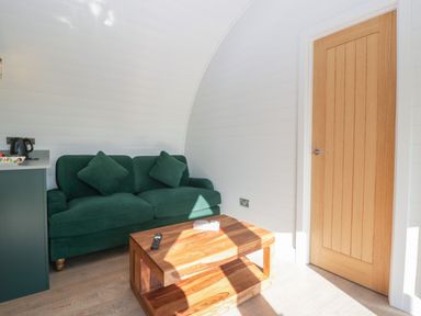 A green sofa with cushions near a wooden coffee table and a wooden door at Leadon View Willow in Upleadon near Newent