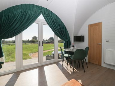 A dining area with a round table and four chairs near glass doors with green curtains at Leadon View Willow in Upleadon near Newent