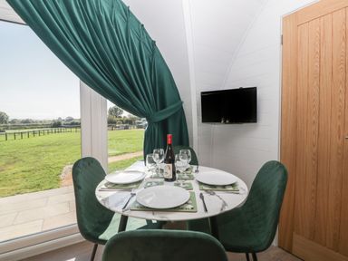 A dining area with a round table set for four near a large window with green curtains at Leadon View Willow in Upleadon near Newent