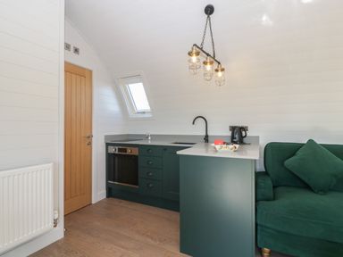 A kitchen area with green cabinets oven and sink next to a green sofa at Leadon View Willow in Upleadon near Newent