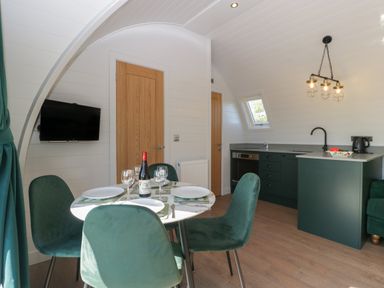 A dining table set for four with green chairs in a kitchen area with wood doors and a mounted TV at Leadon View Willow in Upleadon near Newent